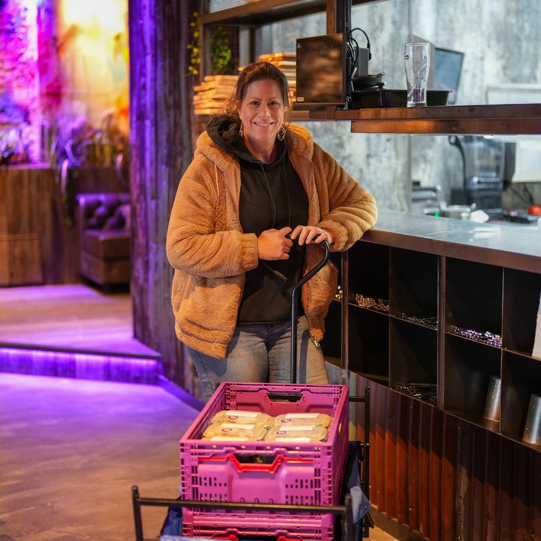 Glimlachende vrouw neemt donatiemaaltijden in ontvangst bij RNGRZ voor kwetsbare buurtgenoten